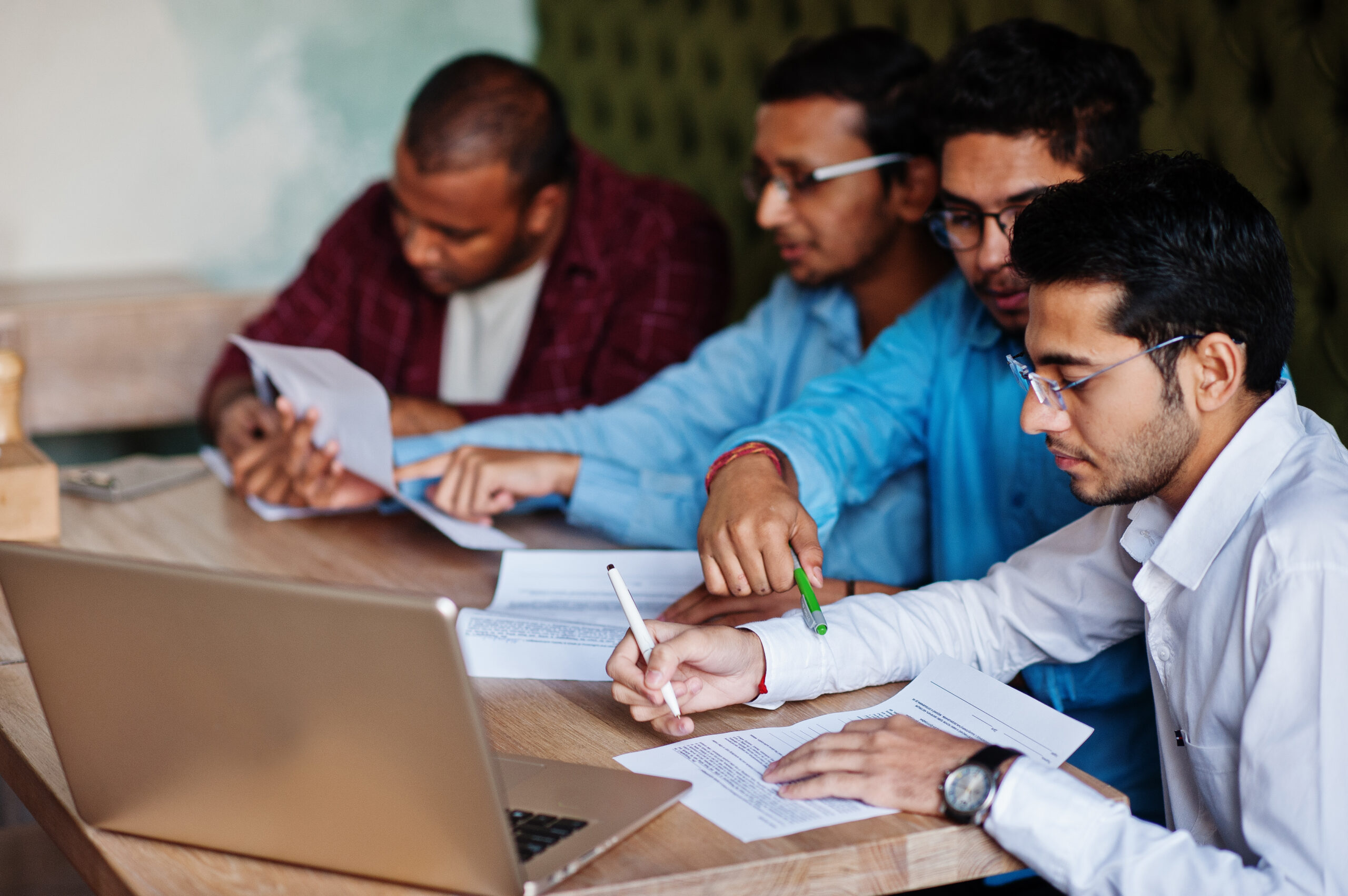 Group of four south asian men's posed at business meeting in cafe. Indians together and sign important documents. Contract to study and work.